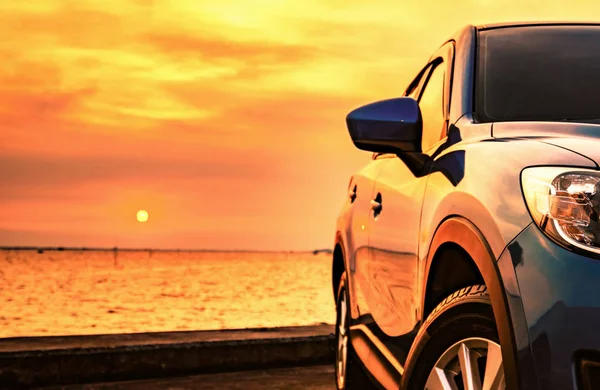 Blue compact SUV car with sport and modern design parked on concrete road by the sea at sunset. Environmentally friendly technology. Business success concept. — Stock Photo, Image