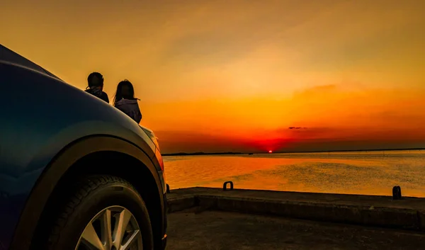 Silhueta de felicidade casal de pé e relaxante na praia em frente ao carro com céu laranja e azul ao pôr do sol. Verão férias e conceito de viagem. Romântico jovem casal namoro à beira-mar . — Fotografia de Stock