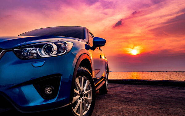 Blue compact SUV car with sport and modern design parked on concrete road by the sea at sunset. Environmentally friendly technology. Business success concept.