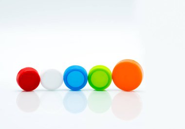 Different size of white, green, red, blue and orange color round plastic screw caps in a line on white background and copy space. clipart