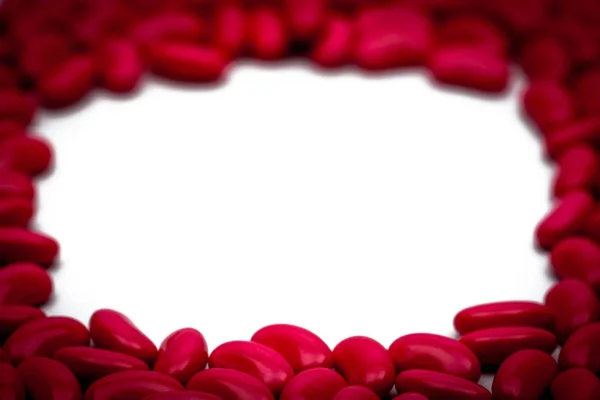 Enfoque selectivo de píldoras recubiertas de azúcar en forma de riñón rojo sobre fondo blanco con espacio de copia — Foto de Stock