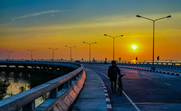 Les gens se détendre sur la route côtière incurvée avec lampadaire et ciel orange au coucher du soleil à Chonburi, Thaïlande . — Photo