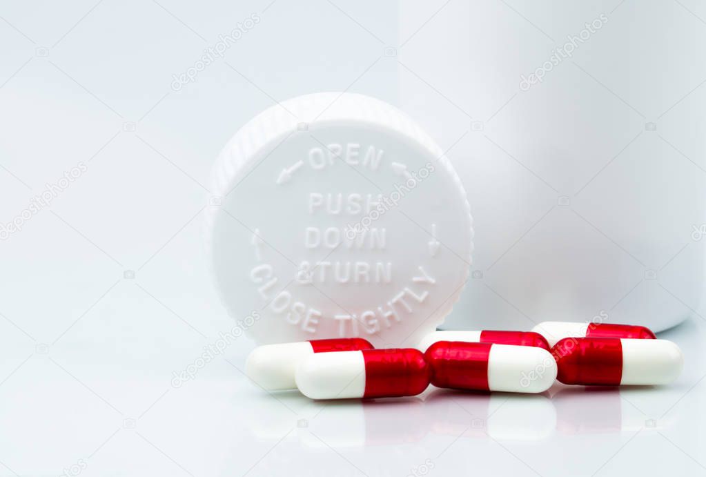 Capsules pills on white background and plastic bottle with blank label and copy space. Childproof packaging. Child resistant pill container. Push down and turn cap. Global healthcare concept.