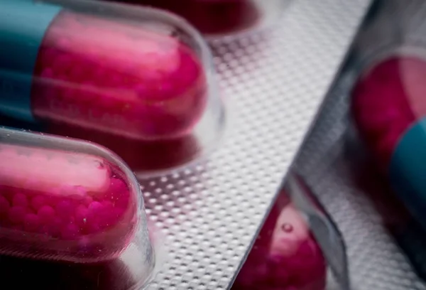 Enfoque selectivo de azul, cápsula rosa con gránulos en píldoras laterales. Pastillas en blíster sobre fondo blanco. Forma farmacéutica de dosificación y embalaje. Medicina antifúngica . —  Fotos de Stock