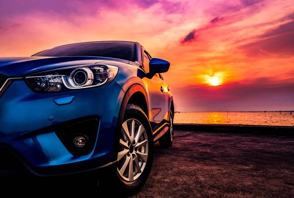 Coche SUV azul compacto con diseño deportivo y moderno estacionado en carretera de hormigón junto al mar al atardecer. Tecnología respetuosa con el medio ambiente. Concepto de éxito empresarial . — Foto de Stock