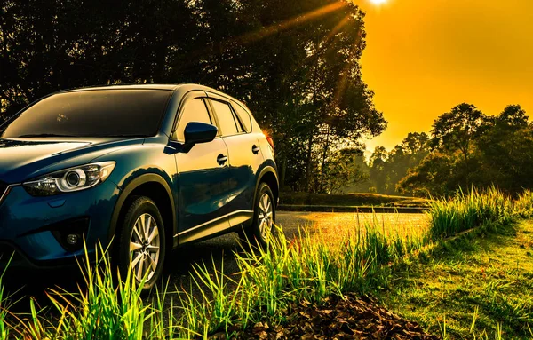 Blue compact SUV car with sport and modern design parked on concrete road at sunrise with orange sky. Environmentally friendly technology. Business success and travel concept. — Stock Photo, Image