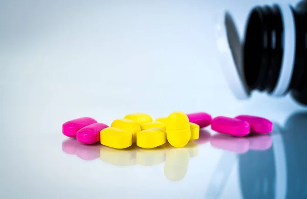 Жовті і рожеві овальні таблетки з тінями на білому тлі з пляшкою розмитих таблеток. Від легкого до помірного болю. Ліки від болю. Пігулки від ібупрофену . — стокове фото