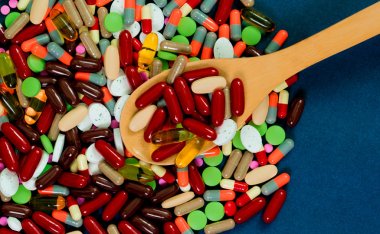 Renkli Tablet ve kapsül hap ve mavi zemin üzerine tahta kaşık yığını. Antibiyotik direnci kavramı. İlaç endüstrisi. Küresel sağlık. İlaç etkileşimleri kavramı