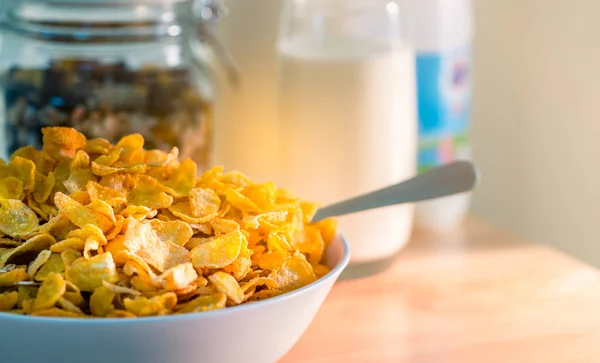 Bowl of cereal with spoon put on wood table near granola in glass container and one glass of milk. Calcium food breakfast for children before go to school in the morning. Cornflakes and milk concept