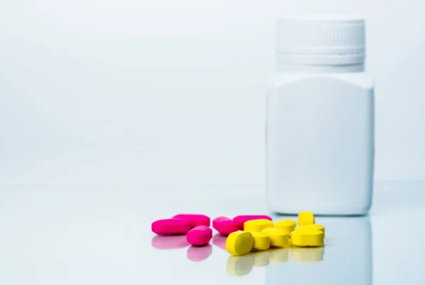 Pile of pink and yellow tablets pills near plastic pills bottle with blank label isolated on white background with copy space. Ibuprofen for relief pain. Pharmaceutical industry and drugstore concept. — Stock Photo, Image