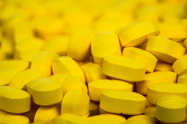 Selective focus on pile of yellow tablets pills . Ibuprofen tablets pills. Painkiller medicine for headache, high fever and anti inflame. Pharmaceutical industry concept. Health policy and budgets. clipart