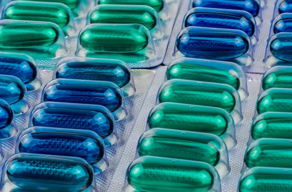 Dettaglio macro shot di capsule di gel morbido blu e verde in blister. Naproxene e ibuprofene (FANS): medicinale antidolorifico. Concetto di industria degli imballaggi farmaceutici . — Foto Stock