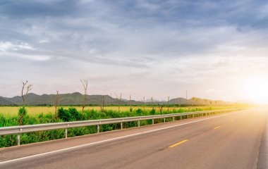 Asfalt yolu yeşil çim tarlası ve güneş ışığıyla kaplı dağın yanında. Mavi gökyüzü ve beyaz bulutla uzun bir yolculuk. Asfalt yolda. Yolculuk konsepti. Doğa manzarası.
