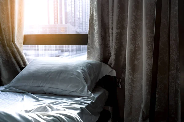 Ranjang nyaman putih dan bantal lembut di kamar tidur modern. Tidur dekat jendela dan tirai di hotel di pagi hari dengan sinar matahari. Lembaran kasur dan sarung bantal. Desain interior kamar tidur. Tidur dengan nyaman . — Stok Foto