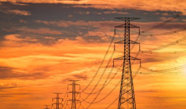 Akşamları yüksek voltajlı elektrik direği ve şanzıman hattı. Gün batımında elektrik direkleri. Güç ve enerji. Dağıtım istasyonunda kabloyla turuncu gün batımı gökyüzü olan yüksek voltaj şebekesi kulesi..