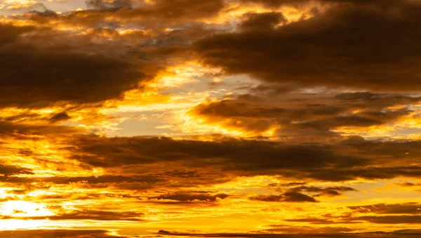 Schöner Himmel bei Sonnenuntergang. Goldener Himmel bei Sonnenuntergang mit schönem Wolkenmuster. Orange, gelb und dunkle Wolken am Abend. Freiheit und ruhiger Hintergrund. Schönheit in der Natur. Mächtige und spirituelle Szene. — Stockfoto