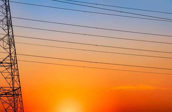 Silhouet hoogspanning elektrische pyloon en elektrische draad met een oranje hemel. Elektriciteitspalen bij zonsondergang. Energie- en energieconcept. Hoogspanningsnettoren met draadkabel bij distributiestation. — Stockfoto