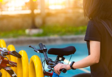 Bisiklet paylaşım sistemleri. Kiralık iş için bisiklet. Asyalı kadın bisiklet parkında bisiklet sürmeye giderken akıllı bant takıyor. Çevre dostu nakliye aracı. Kentsel ekonomi toplu taşımacılık.