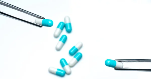 钳从一组胶囊药丸中挑选白蓝色胶囊 药物选择 抗生素的选择 抗生素耐药性概念 药厂概念中的质量保证和质量控制 选择的药物 — 图库照片
