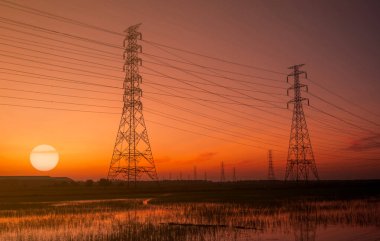 Yüksek voltajlı elektrik direği ve günbatımı gökyüzüne sahip elektrik kablosu. Elektrik direkleri. Güç ve enerji kavramı. Kablo kablolu yüksek voltaj şebekesi kulesi. Güneşin batışında kırmızı-turuncu gökyüzü.