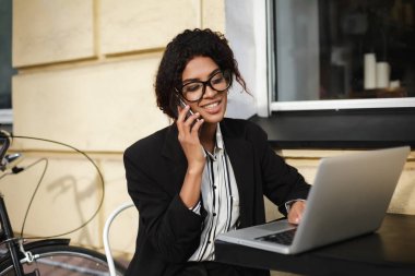 Kafeterya masada oturan ve dizüstü bilgisayarda çalışma gözlük gülümseyen Afro-Amerikan kız portresi