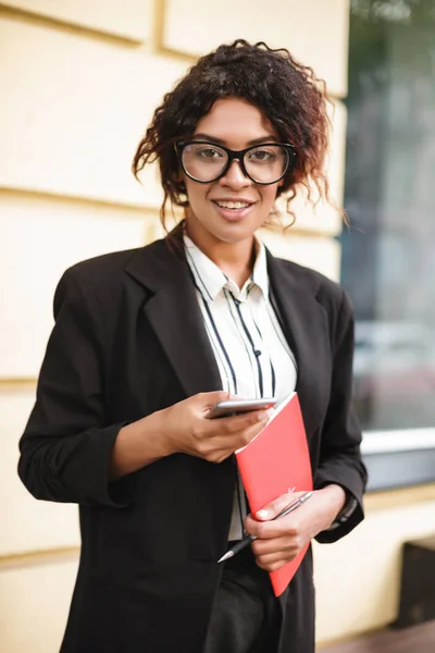 Porträt eines lächelnden afrikanisch-amerikanischen Mädchens mit Brille, das mit dem Handy in der Hand glücklich in die Kamera blickt — Stockfoto