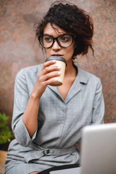 Портрет афро-американських дівчинка в окулярах сидіти на лавці і пити каву дивлячись мрійливо сторону — стокове фото