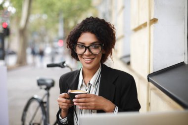 Kafeterya masada oturan ve kahve elinde tutan gözlük gülümseyen Afro-Amerikan kız portresi