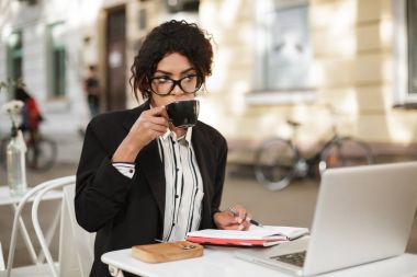 Kafeterya masada laptop ve defter ile masaya oturan gözlüklü Afro-Amerikan kız portresi