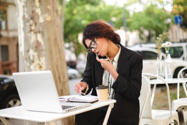 Kafeterya masada oturan ve çalışırken cep telefonunu konuşurken gözlüklü Afro-Amerikan kız portresi