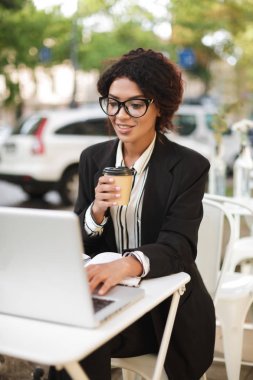 Kafeterya masada oturan ve onu laptop çalışma gözlük gülümseyen Afro-Amerikan kız portresi
