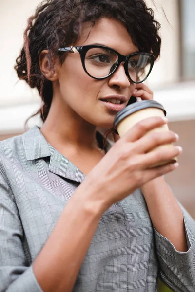 Retrato de menina afro-americana em pé óculos e falando em seu celular com café nas mãos — Fotografia de Stock