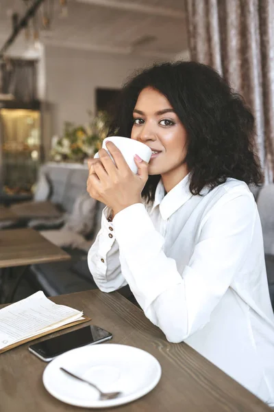 Gadis muda Afrika-Amerika duduk di restoran dengan secangkir kopi di tangan — Stok Foto