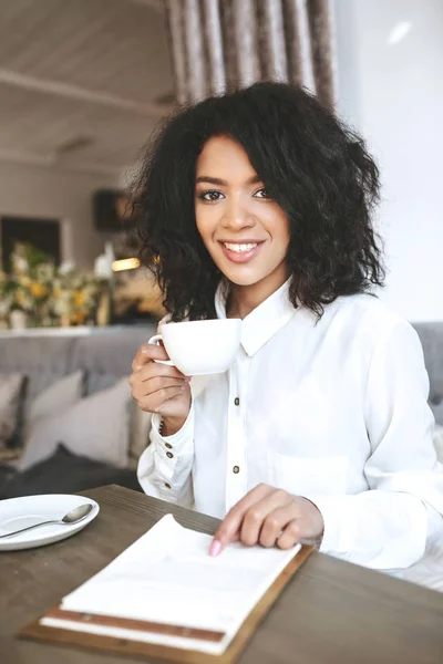 Gadis muda Afrika-Amerika duduk di restoran dengan secangkir kopi — Stok Foto