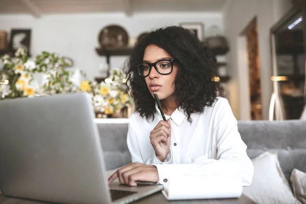 Joven chica afroamericana trabajando en el ordenador portátil en restaurante.Pretty chica con pelo rizado oscuro sentado en la cafetería con el ordenador portátil — Foto de Stock