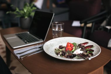 Restoranda masada çatal ile salata, dizüstü bilgisayar ve su ve bıçak fotoğrafını ekrana yakın