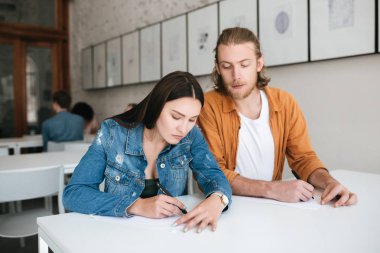 Genç adam dikkatle onun sınıf arkadaşı testine ders üzerinde gözetleme. Düşünceli test yazma ve el ile kapatma ciddi kız