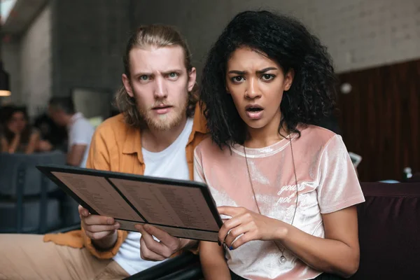 Shocked chica afroamericana con el pelo rizado oscuro y chico con el pelo rubio asombradamente mirando en la cámara en el café —  Fotos de Stock