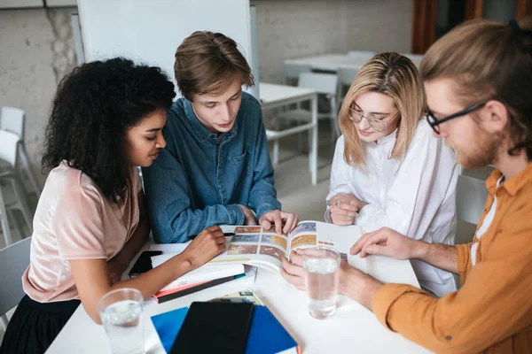 Grupo de jóvenes sentados a la mesa y trabajando juntos. Retrato de dos chicas guapas y dos chicos discutiendo algo —  Fotos de Stock