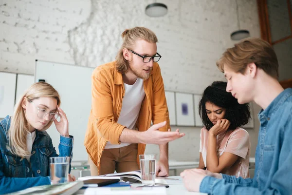 Adam sarı saçlı ve masanın üzerine eğilerek ve öğrenciler için bir şeyler açıklamaya sakal portresi