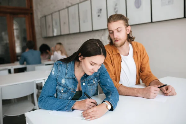Genç adam onun sınıf arkadaşı testine gözetleme portresi. Ciddi kız düşünceli sınav el ile kapatma süre yazma