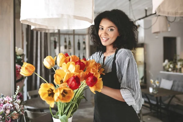 Florist indah di celemek bekerja dengan bunga. Gadis muda Afrika-Amerika membuat karangan bunga tulip — Stok Foto