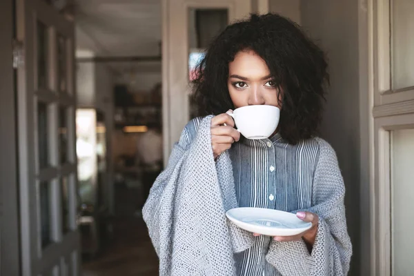 Menina afro-americana agradável beber café embrulhado em xadrez. Senhora bonita com cabelo encaracolado escuro de pé com xícara de café no restaurante — Fotografia de Stock