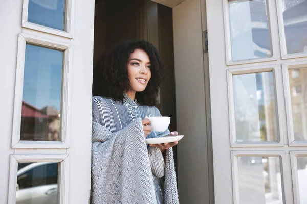 Neşeli Afro-Amerikan kız restoranda kahve içme. Siyah kıvırcık saçlı konumu olan genç kız elinde Kupası ile ekose içinde sarılmış