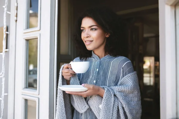 Retrato de hermosa dama envuelta en cuadros con taza de café en las manos. Linda chica afroamericana bebiendo café en el restaurante — Foto de Stock