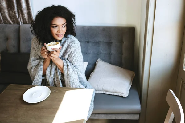 Gadis muda Afrika-Amerika minum kopi di restoran. Potret wanita baik dengan rambut keriting gelap bermimpi melihat keluar jendela dengan cangkir di tangan — Stok Foto