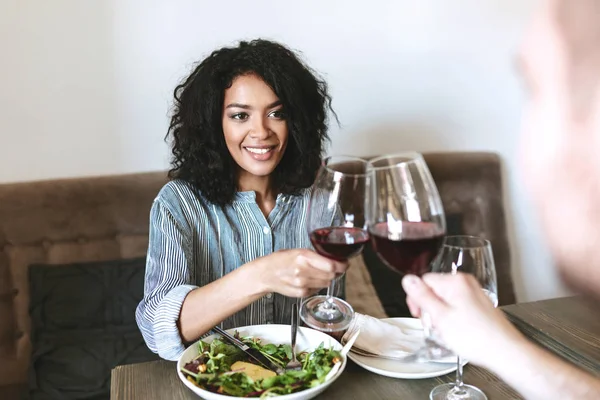 Retrato de una joven afroamericana en restaurante con copa de vino tinto en la mano y ensalada en la mesa — Foto de Stock