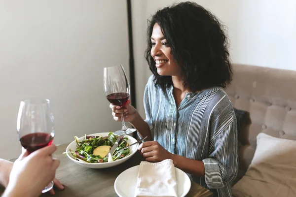 Retrato de la hermosa chica afroamericana con copa de vino tinto en la mano y ensalada en la mesa en el restaurante — Foto de Stock