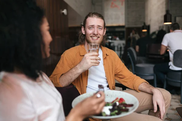 Smiling man sitting in restaurant and talking with girl. Boy sitting at cafe with glass of water in hand