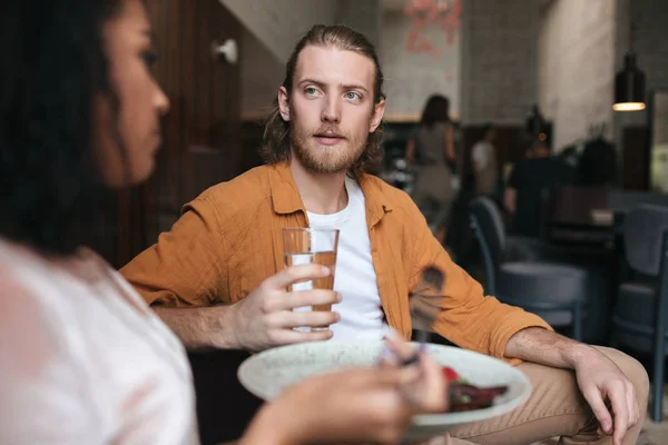 Young man sitting in restaurant and talking with girl. Boy sitting at cafe with glass of water in hand — Stock Photo, Image